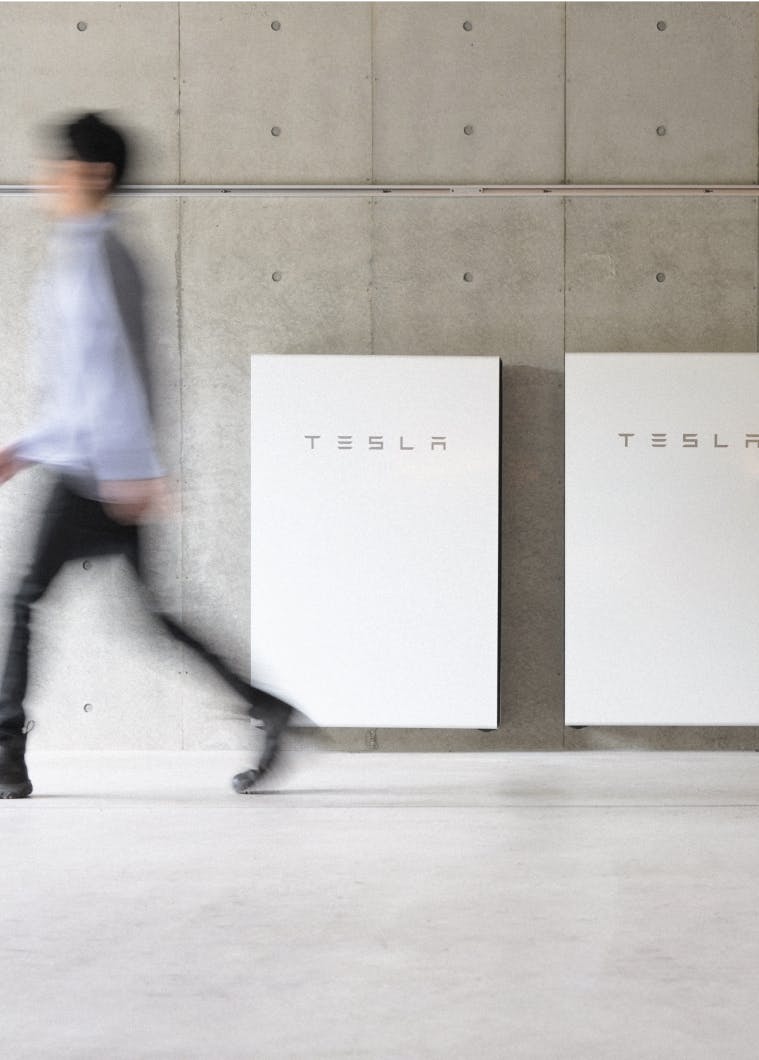Man passing by Tesla batteries on a wall